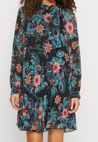 Svart blommig klänning med långa ärmar, utsmyckad med färgglada blommönster i rosa, blått och grönt. Inkluderar en knytning vid halsen.