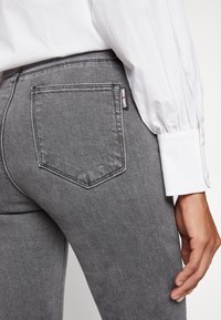 Jean en denim gris avec une coupe ajustée, doté d'une poche arrière et d'une étiquette de marque. Le tissu a une texture lisse et une légère usure.