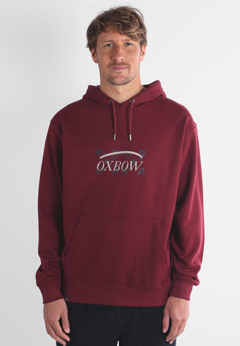 Haut à capuche bordeaux en tissu doux, avec une poche avant, une capuche à cordon et un logo avec des éléments décoratifs en bleu.