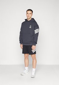 Mørkegrå hettegenser med hvit tre-stripete design på armene, kengurulomme, sammen med svarte shorts med hvite detaljer.