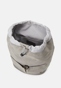 Borsa a sacco in tela grigia con fodera a righe, apertura con cordoncino, tasca frontale e dettagli in metallo. L'esterno è liscio; l'interno è texturizzato.