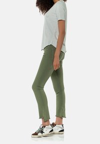 Camiseta de manga corta gris claro, jeans skinny verde oliva con dobladillos sin terminar y zapatillas blancas con acentos marrones y cordones de colores.