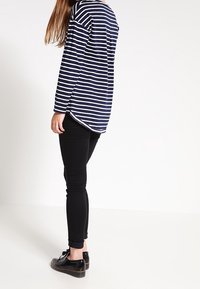 Marinblå och vit randig långärmad skjorta med rundad nederkant, kombinerad med svarta skinny jeans och svarta snörskor.