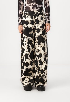 Szerokie spodnie z nadrukiem w czarno-białe łatki przypominające wzór krowy, noszone z czarnymi butami na masywnej podeszwie oraz dopasowaną bluzą z długim rękawem.