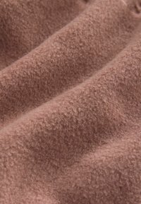 Weiches, strukturiertes pinkes Gewebe mit leicht flauschigem Aussehen, das sanfte Wellen und Variationen in der Farbnuance über die gesamte Oberfläche zeigt.