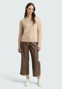 Helles beige gestricktes Sweatshirt mit einem gerippten unteren Saum, kombiniert mit braunen, weiten Hosen aus Kunstleder und weißen Sneakers.