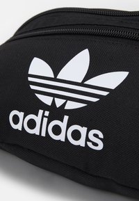 Black zippered pouch made of textured material, featuring a prominent white Adidas logo with three leaf design and three horizontal stripes.