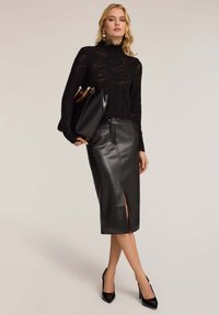 Svart stickad topp med hög krage, kombinerad med en svart läder pennkjol med en sidofissur, och svarta spetsiga klackar.