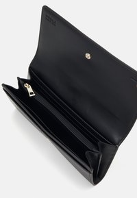 Portafoglio in pelle nera con più scomparti per carte, un vano con zip e chiusura a pressione. Presenta un logo discreto impresso all'interno.