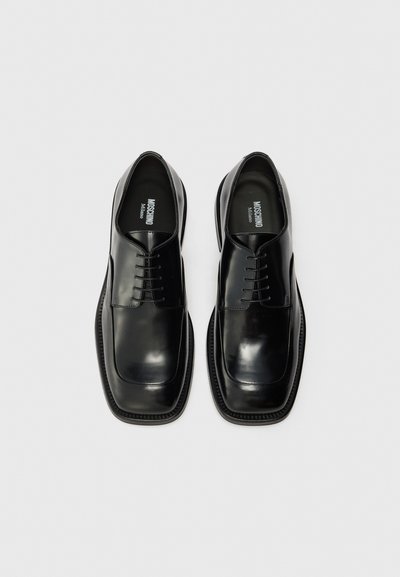 Black leather dress shoes with a glossy finish, square toe, lace-up design, and decorative stitching along the sole edge.