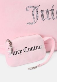 Pochete de veludo rosa com "Juicy Couture" em letras prateadas, fecho em zíper e alça de corrente prateada com clipe. Textura suave, design compacto.