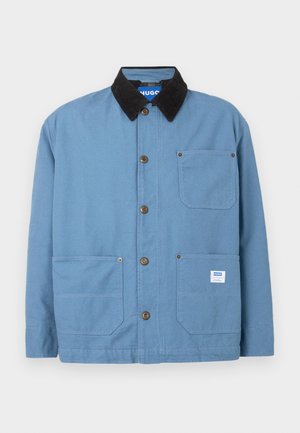 Blauwe canvas jack met een zwart corduroy kraag, borstzak, twee voorzakken en bruine knoopsluitingen. Beschikt over een merklabel aan de binnenkant.