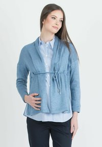 Světle modrý pletený cardigan s páskem na zavázání, otevřeným předním dílem a dlouhými rukávy, nosí se over modro-bílým pruhovaným tričkem. Měkká textura.