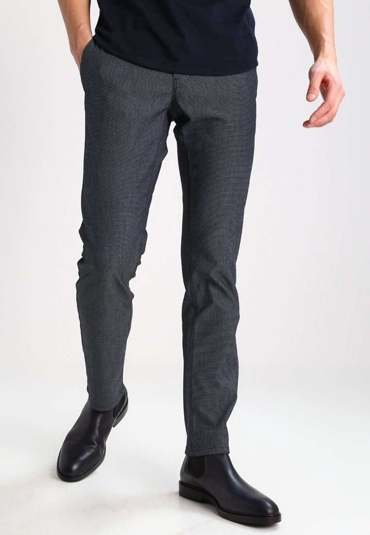 Grå mönstrade byxor med smal passform, tillverkade av textil med struktur. Matchas med svarta läderankelstövlar. Framtida fickor med skräddarsytt utseende.