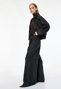 Donker gestreepte jas met een kraag, gecombineerd met een bruine coltrui en hoge, wijde broek, geaccentueerd met een riem.