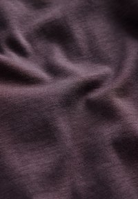 Gros plan sur un tissu texturé violet foncé avec des plis doux et un motif de tissage visible.