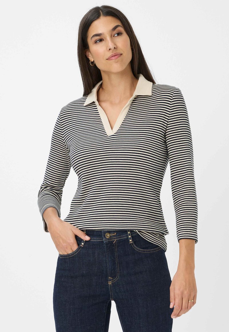 Gestreiftes Langarmshirt mit V-Ausschnitt und beigem Kragen; der Stoff ist weich und weist marineblau- und cremefarbene Streifen auf; kombiniert mit dunklen Jeans.