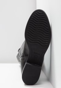 Semelle de botte en cuir noir avec une bande de roulement en caoutchouc à motif et un talon, montrant le nom de la marque Geox en dessous.