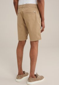 Khaki shorts with a regular fit, made of soft cotton, featuring back pockets and a small logo on the rear. Worn with light brown suede shoes.
