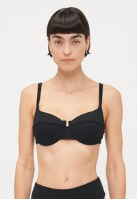 Čierny bikiny top s vypchávkami, širokými ramienkami a detailom stredového švu. Hladká textúrovaná tkanina, minimalistický dizajn.
