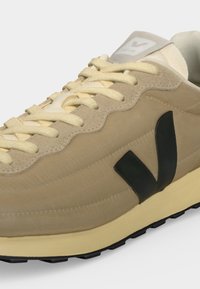 Baskets beige avec lacets crème, logo "V" noir sur le côté, semelle beige clair et languette en mesh avec marquage Veja.