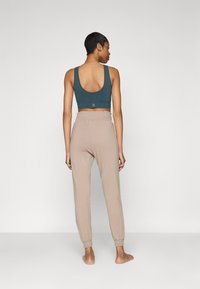 Top cortissimo teal con spalline larghe e scollo a goccia, abbinato a pantaloni jogger beige chiaro con vita elastica e polsini a costine.