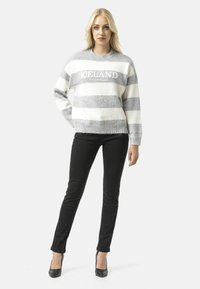 Chandail rayé gris et blanc avec le texte "ICELAND". Matériau en maille, col rond, coupe décontractée, associé à un jean skinny noir et des talons.