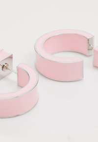 Boucles d'oreilles en émail rose en forme courbée, avec une finition lisse et brillante et des bordures en argent. Fermeture avec tige ajustable.