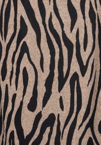 Stickad textil med en beige bakgrund och djärva svarta zebraränder. Designen inkluderar varierande linjebredder som skapar ett strukturerat mönster.