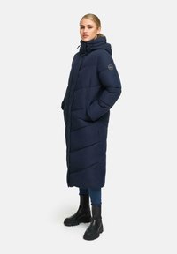 Marineblauwe lange pufferjas met capuchon, voorzien van een gestikte afwerking en zijzakken. Draag het over denim en zwarte chunky laarzen.