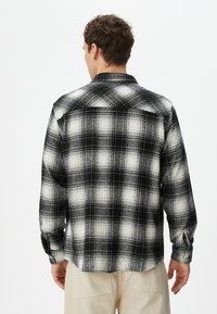 Sorte og hvide ternede flannel skjorte, lange ærmer, knap-til-ned krave, struktureret stof, synlige sømme, med en buet kant bagpå.