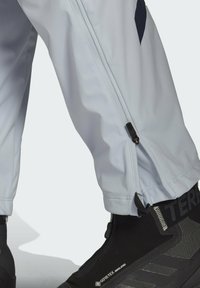 Pantalones impermeables de color gris claro con detalles de cremallera en el tobillo, combinados con calzado aislante de Gore-Tex negro con acentos texturizados.