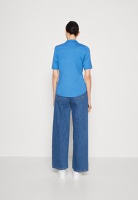 Blue short-sleeve top with a collar and curved hem, paired with wide-leg denim jeans. Simple design with a smooth texture.