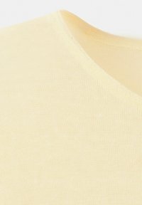 Prim-plan cu material tricotat moale, de culoare crem, evidențiind textura fină și cusătura curbată a decolteului.