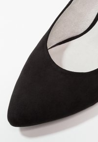 Chaussure en suède noir à bout pointu avec une texture lisse, découpes arrondies pour la cheville et un subtil éclat sur la surface supérieure.