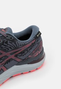 Chaussure de course gris foncé et rose avec semelle amortissante FlyteFoam et étiquette Gore-Tex sur le col rembourré de la cheville.