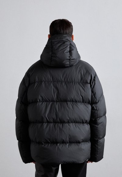 Chaqueta acolchada negra con capucha, que presenta un diseño acolchado y una textura gruesa y suave. La parte trasera muestra secciones esponjosas distribuidas uniformemente.