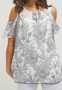 Huitu valkoinen pusero, jossa on kylmät olkapäät, mustia kukkakuvioita, pyöreä kaula-aukko, avainreikäyksitys ja musta reunus helman ympärillä.