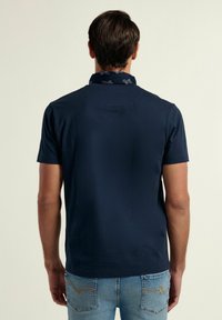 Camisa polo de manga corta en azul marino con collar, que presenta un escote con patrón. La tela parece suave y ligera.