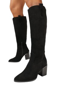 Bottes en suède noir jusqu'au genou avec un bout pointu, un talon épais, une fermeture éclair sur le côté et des languettes en haut pour un enfilage facile.