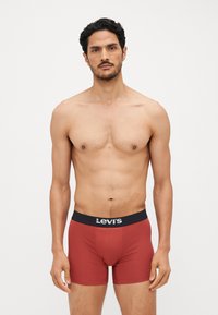 Boxer-briefs en coton rouge avec une ceinture en logo Levi's noir, design ajusté et texture lisse. Portés par un homme avec un torse nu.