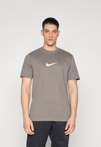 Camiseta de cuello redondo gris hecha de algodón con mangas cortas, que presenta un destacado logo en blanco de Nike en el pecho.