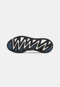 Sort og hvid sneakersål med blå grebsektioner og zigzag mønster for trækkraft, fotograferet på en hvid baggrund.
