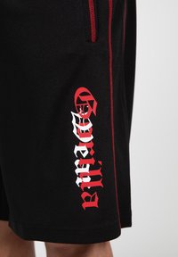 Zwarte shorts van textuurstof, met rode accenten en een grafisch logo in wit en rood op het linkerbeen, voorzien van een ritszak.