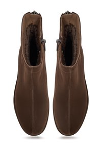 Un par de botas de ante marrones a mitad de tobillo con cremalleras laterales y forro de pelo suave, vistas desde arriba sobre un fondo blanco.