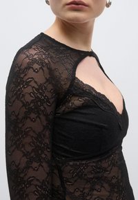 Μαύρο κορμάκι από δαντέλα με βαθύ V στο ντεκολτέ, μακριά ημιδιάφανα μανίκια και λεπτομερή ανθικά μοτίβα. Διαθέτει εφαρμοστή γραμμή και υφασμάτινη υφή.