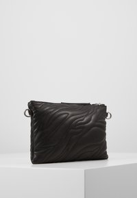 Svart läderväska med kviltat vågmönster, med en silverfärgad dragkedja och cirkulära metallaccenter. Rektangulär form och slät textur.