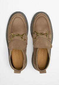 Braune Wildlederslipper mit einem silbernen Kettendetail, schwarzen Gummisohlen und beigem Nähen. Verfügt über eine Zuglasche an der Ferse für einfaches Anziehen.