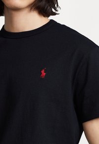 Svart T-shirt i bomull med ribbad rundhalsringning. Har en liten röd broderad logotyp på vänster bröst. Kortsleeves.