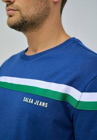 Sudadera de cuello redondo azul con rayas blancas y verdes. "Salsa Jeans" bordado en la parte delantera en blanco. Tela de algodón con textura suave.